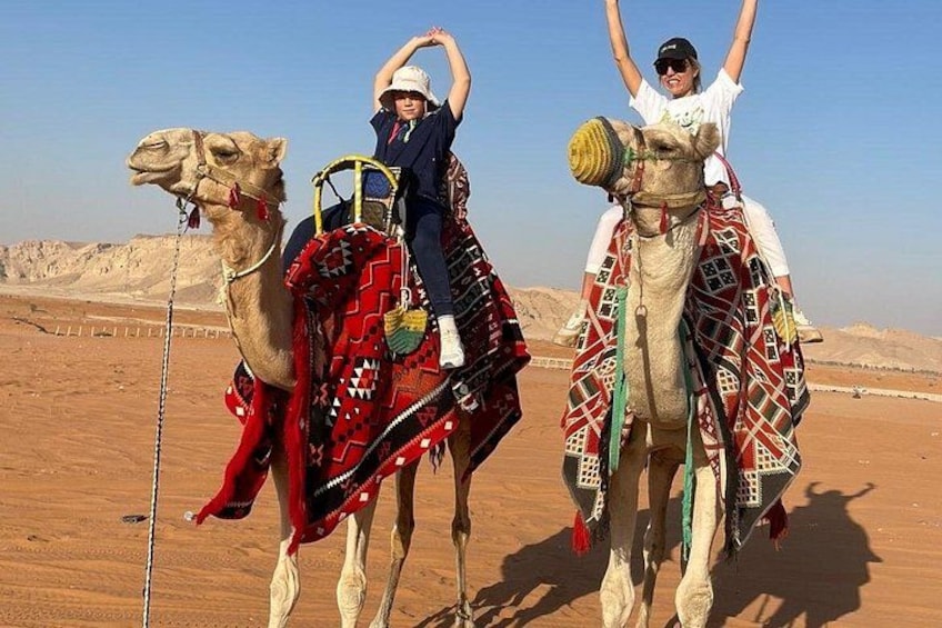 Two camels with riders in a desert landscape. 4