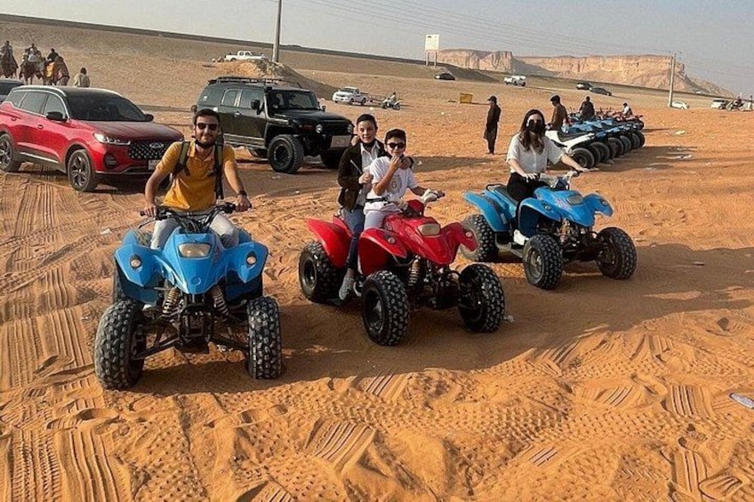 People riding quad bikes in a desert with vehicles and people in the background. 5