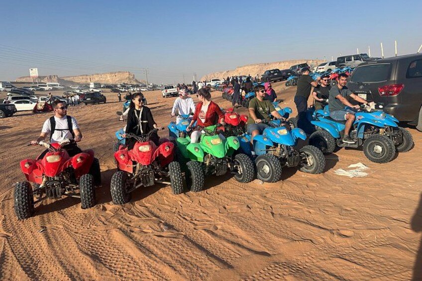 People riding ATVs in a desert setting with vehicles and a clear sky. 3