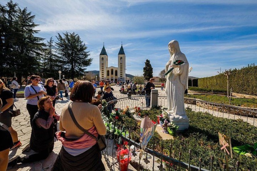 A statue of a robed figure, a church with two towers, and a crowd of people. 1