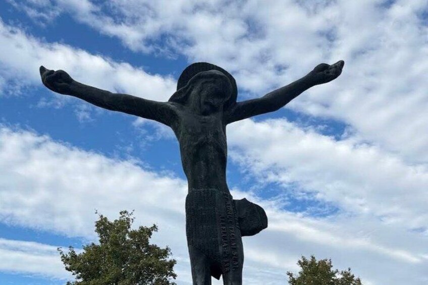 En statue af en figur med udstrakte arme foran en skyet himmel. 3