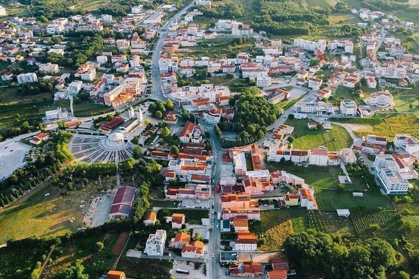 An aerial view of a town with a central roundabout, residential buildings, and surrounding greenery. 2