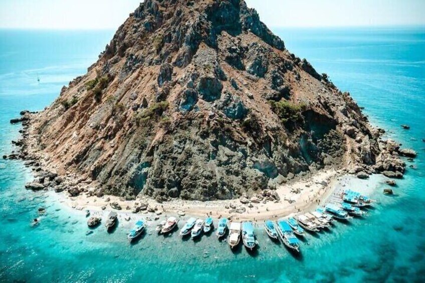 Een rotsachtig eiland omgeven door turquoise water, met verschillende boten afgemeerd bij de kust. 1
