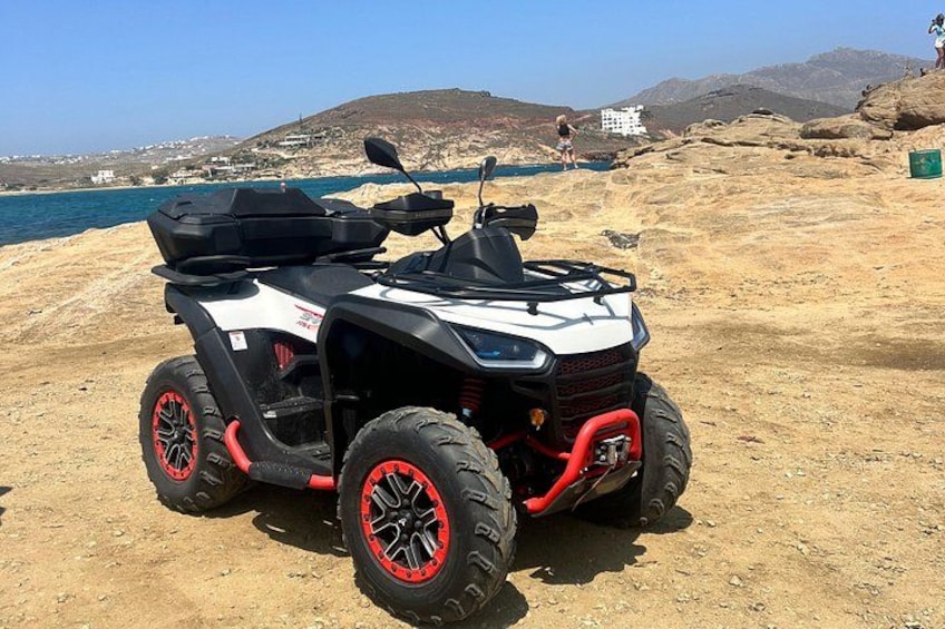 A quad bike parked on a sandy beach with a mountainous backdrop and a body of water. 3