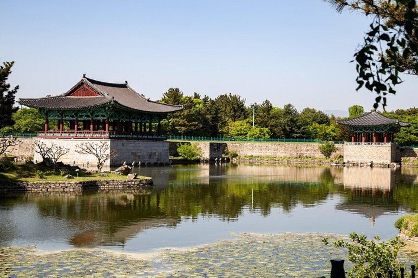 A traditional Korean pavilion by a calm pond with a stone bridge and lush greenery. 3