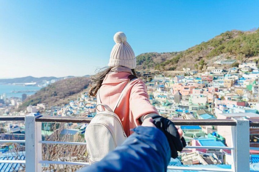 A person in a pink jacket and white beanie overlooking a coastal town with colorful houses. 2
