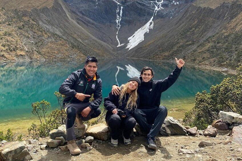 Three people sitting on rocks with a mountain and a lake in the background. 4