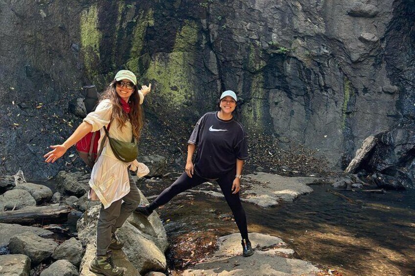 Two people posing by a rocky stream with a cave in the background. 4