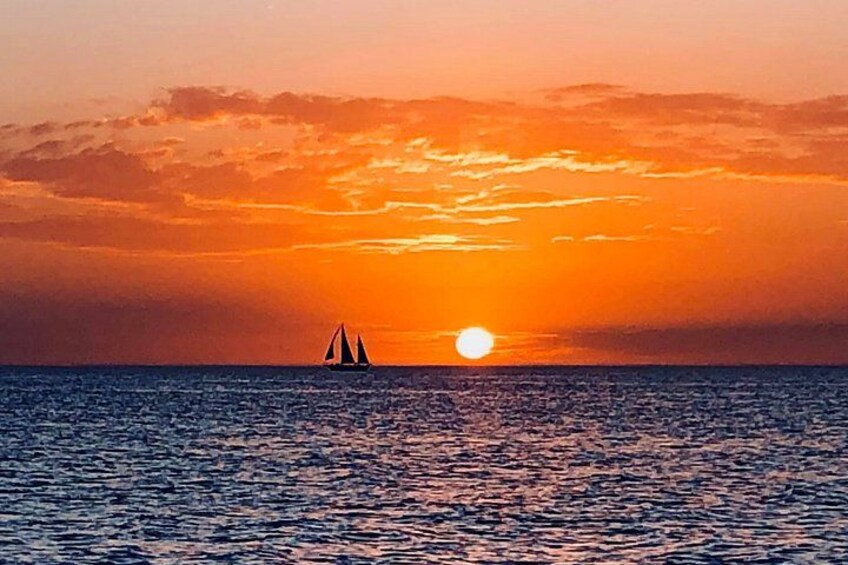 Een zonsondergang boven de oceaan met een zeilboot in de verte. 2