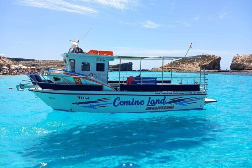 Un barco llamado 'Comino Land' con una costa rocosa al fondo. 1