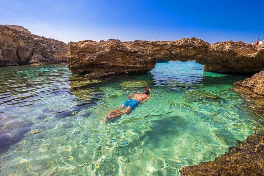 A person snorkeling in clear water under a rocky arch. 2