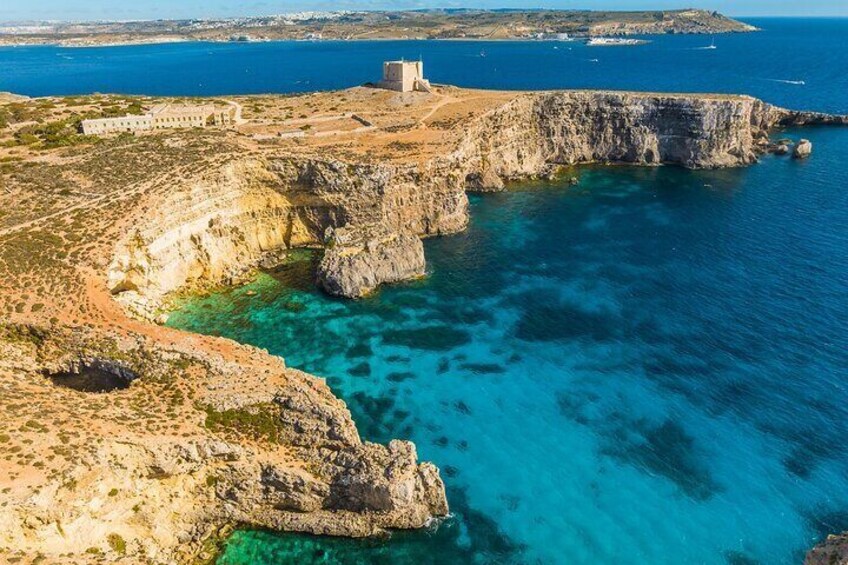 Une falaise côtière surmontée d’un bâtiment, des eaux d’un bleu limpide et une côte lointaine. 2