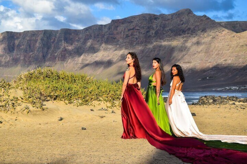 Three women in flowing dresses on a beach with a mountainous backdrop. 3