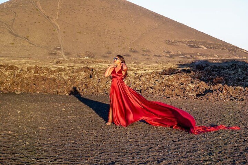 A person in a red dress standing on rocky terrain with a mountainous background. 4