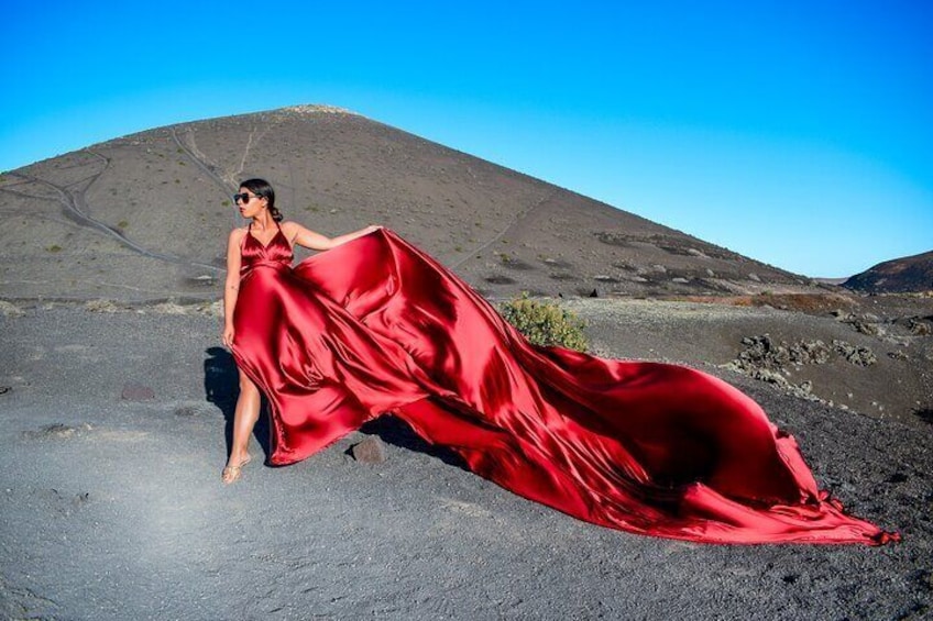 A person in a red dress standing on a rocky terrain with a clear sky. 1