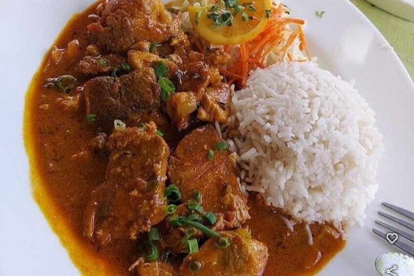 A plate of curry with meat and rice, garnished with herbs. 4
