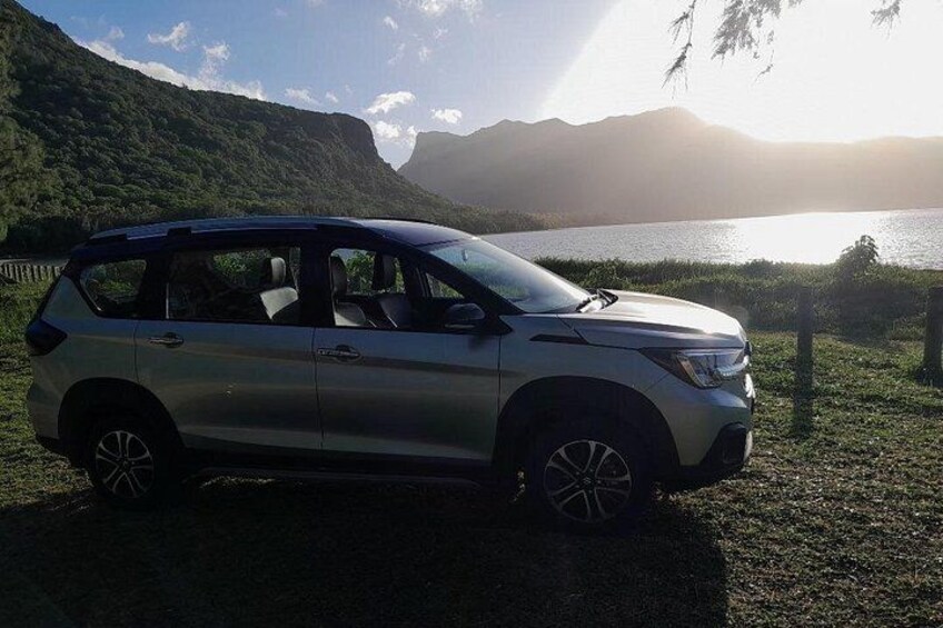 A silver SUV parked on a grassy area near a body of water with mountains in the background. 1