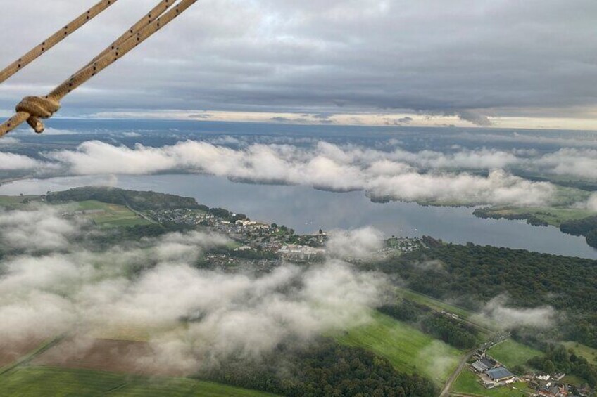 An aerial view of a lake surrounded by clouds, with a town and green fields below. 1
