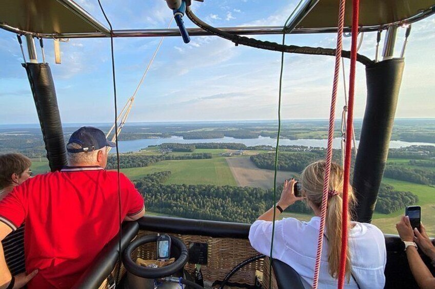 En varmluftsballon med passagerer, der nyder udsigten over et landskab med marker og et vandareal. 1