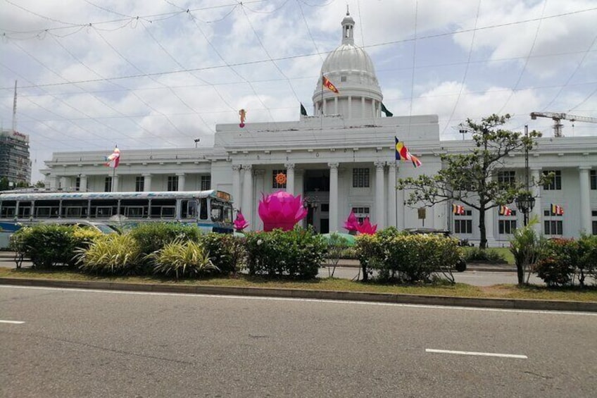 A white building with a dome and flags, surrounded by bushes and a pink sculpture. 3