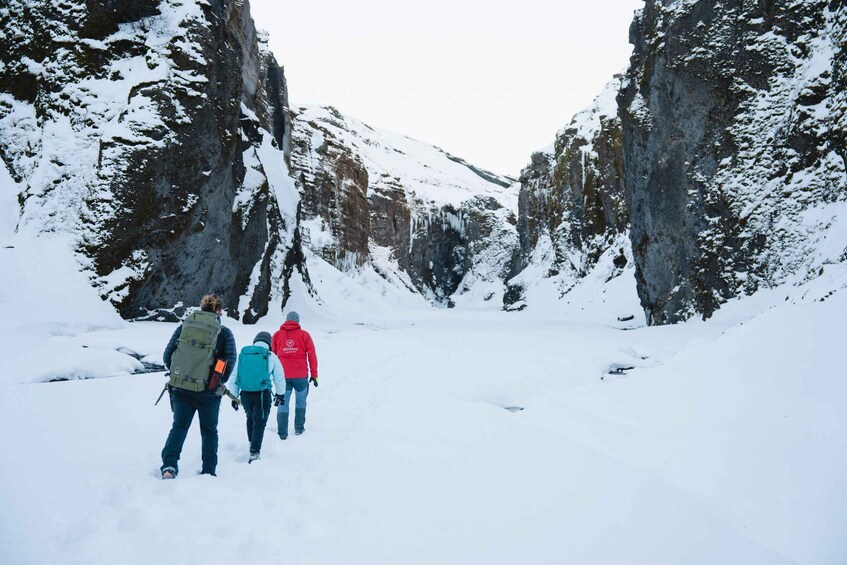 A group of hikers walking on a snow-covered trail between rocky cliffs. 2
