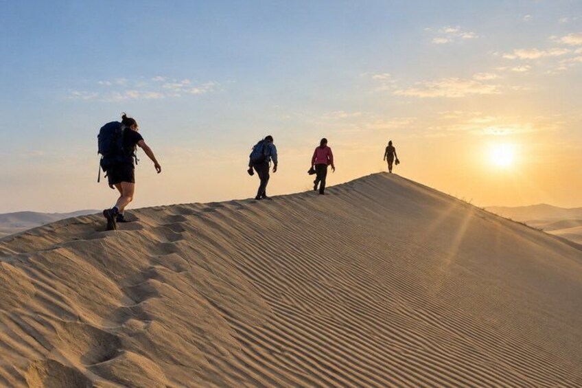 Four people hiking on a sand dune with the sun setting in the background. 1