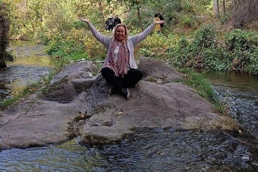 A person sitting on a rock by a flowing river in a wooded area. 3