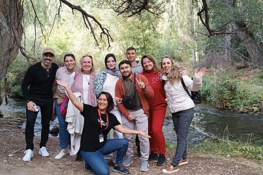 A group of people posing in a forested area with a stream. 1