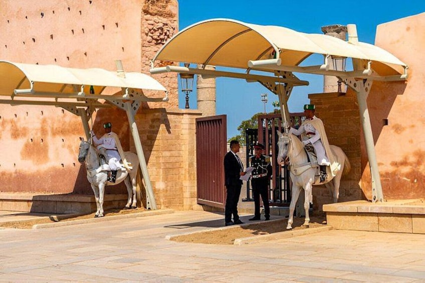 A historical site with two white horses under a canopy, a man in uniform, and a building with a stone facade. 5