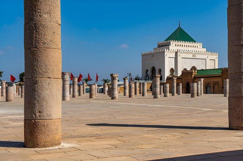 A historical square with columns, a central building with a green roof, and red flags. 3