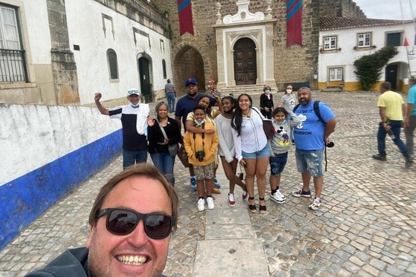 Een groep mensen voor een historisch gebouw met een geplaveid straatje. 1
