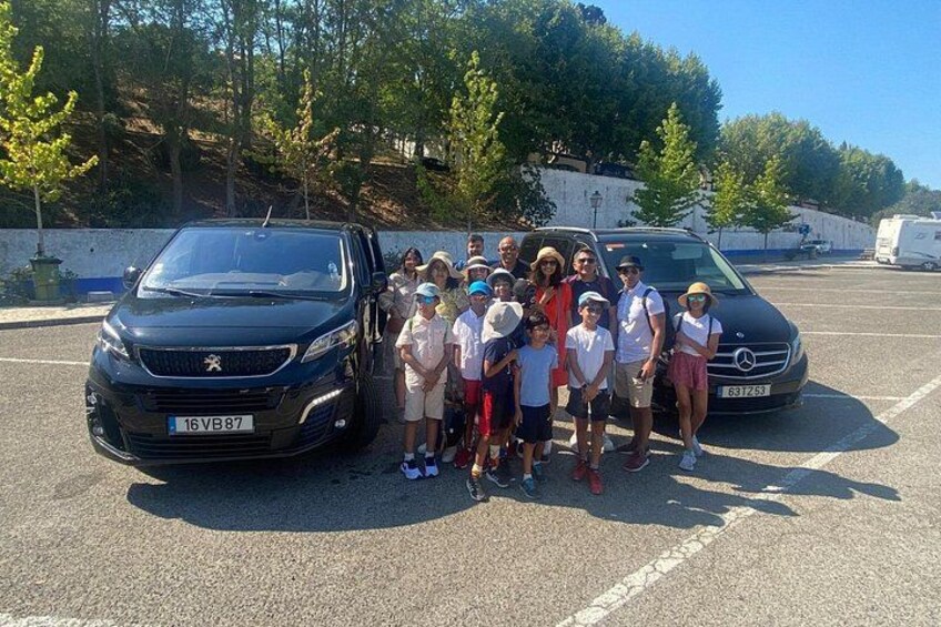 Een groep mensen staat in een parkeerplaats met twee auto's. 2