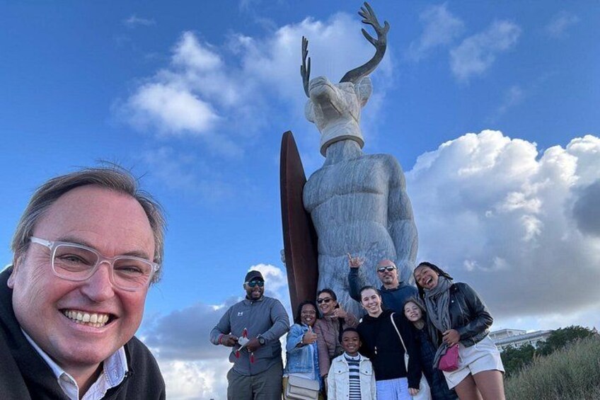 Een groep mensen poseert voor een groot beeld van een figuur met uitgestrekte armen. 3