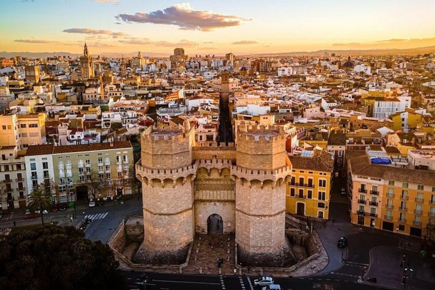 A historic tower with two prominent towers, surrounded by a densely packed urban area with various buildings and streets. 1