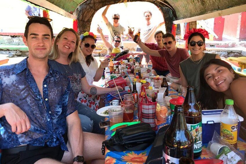 Een groep mensen zit aan een tafel met verschillende flessen en etenswaren. 5