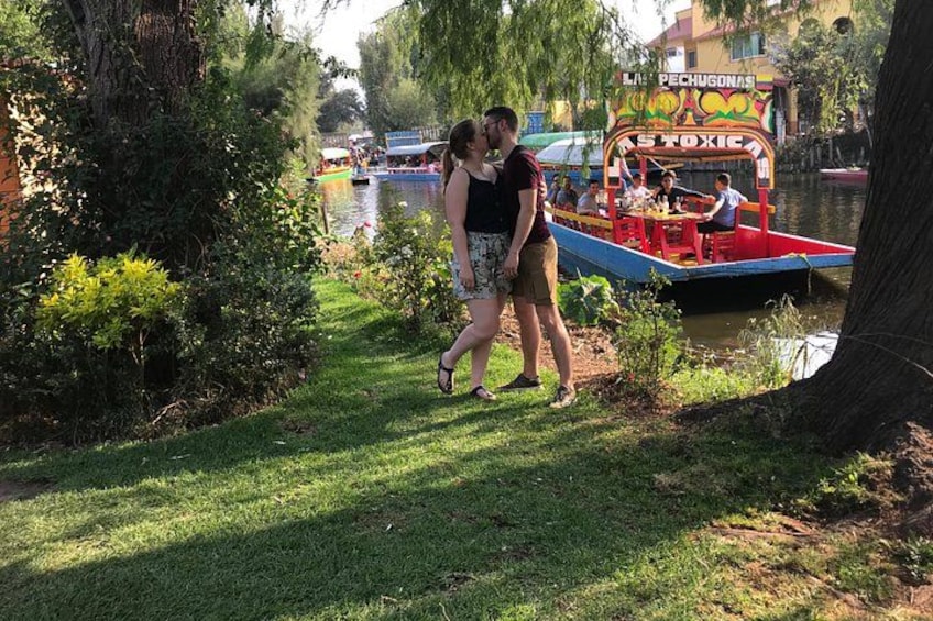 Een stel loopt over een graspaadje langs een rivier, met een kleurrijke boot op de achtergrond. 4