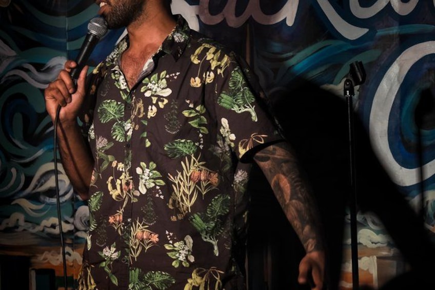 A person holding a microphone, wearing a floral shirt, with a microphone stand in front. 4