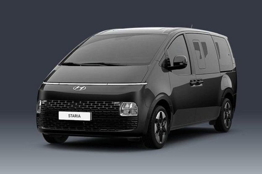 A black van with the brand 'STARIA' on the front grille, a Hyundai logo, and a license plate. 3