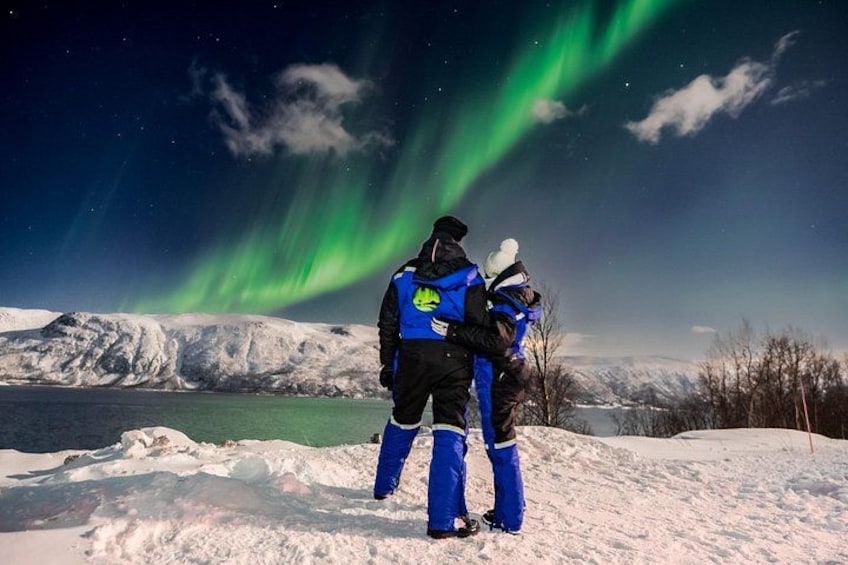 Deux personnes se tiennent debout dans un paysage enneigé, contemplant les aurores boréales. 2