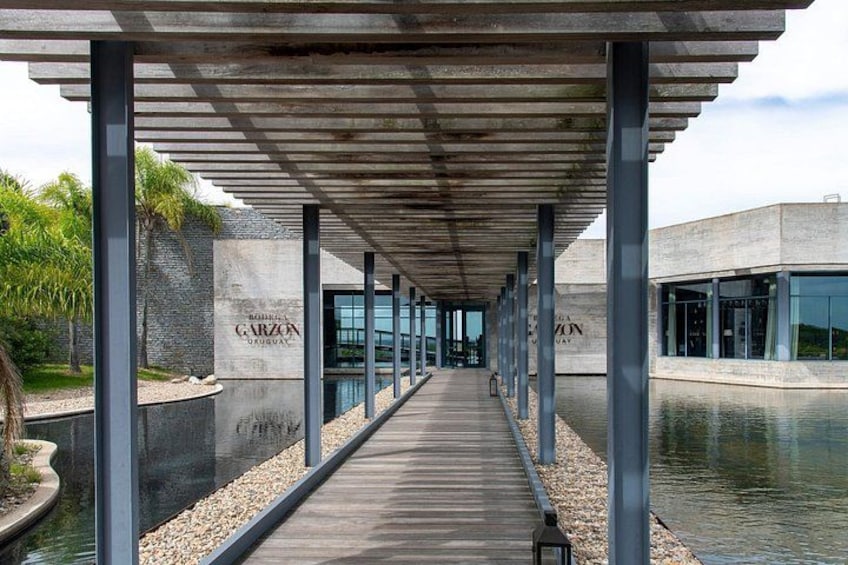 Une allée couverte, agrémentée de chaque côté d’un élément décoratif aquatique, mène à un bâtiment aux fenêtres en verre. 4