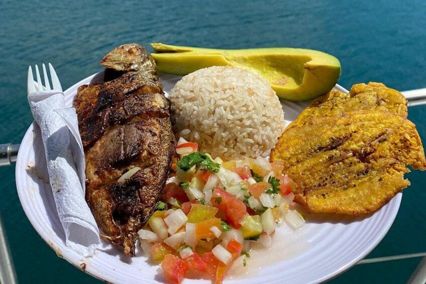 Ein Teller mit gegrilltem Fisch, Reis, einer Avocado-Scheibe, gebratenen Kochbananen und Salsa. 4