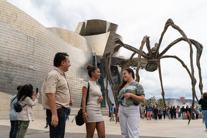 Een groot metalen sculptuur van een spin voor een modern gebouw met een gebogen gevel. 1