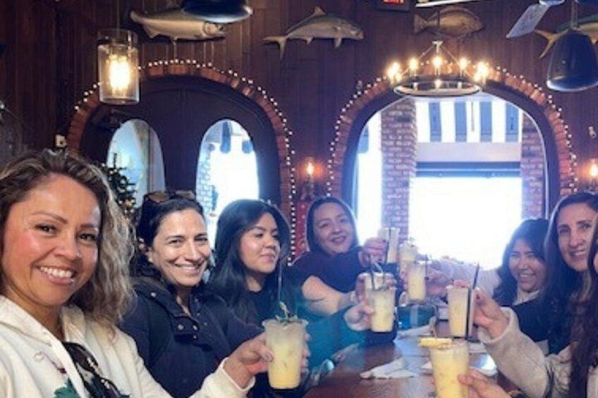 Un grupo de personas brindando con bebidas en un restaurante con paredes de ladrillo abovedadas y luces colgantes. 2