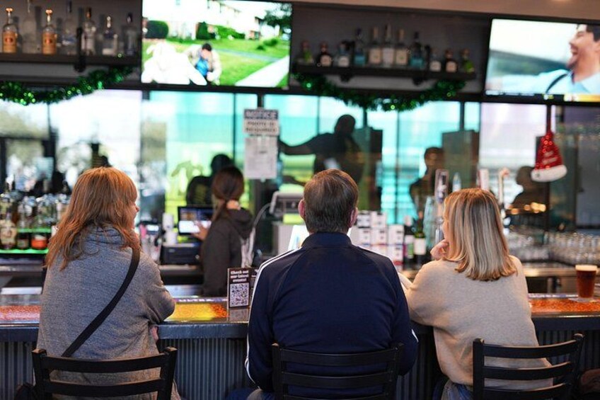 A bar with people seated at the counter, a television screen, and shelves with bottles. 2