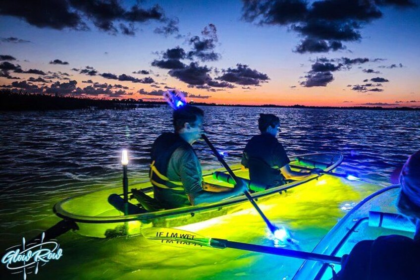 Twee mensen roeien in een boot bij zonsondergang, met kleurrijke lichtjes. 4