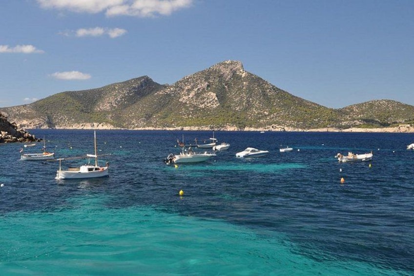 A coastal scene with boats anchored in clear blue waters, surrounded by rocky hills. 2