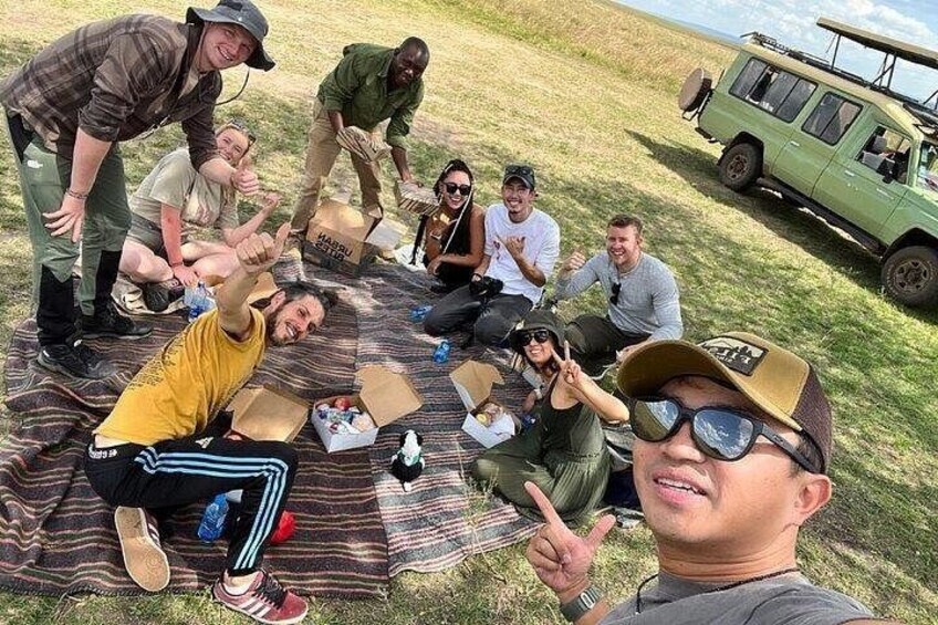 A group of people sitting on a blanket outdoors with a green vehicle in the background. 2