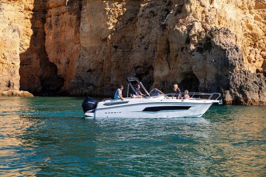 A white motorboat named 'KARNO' on calm water near a rocky cliff. 2