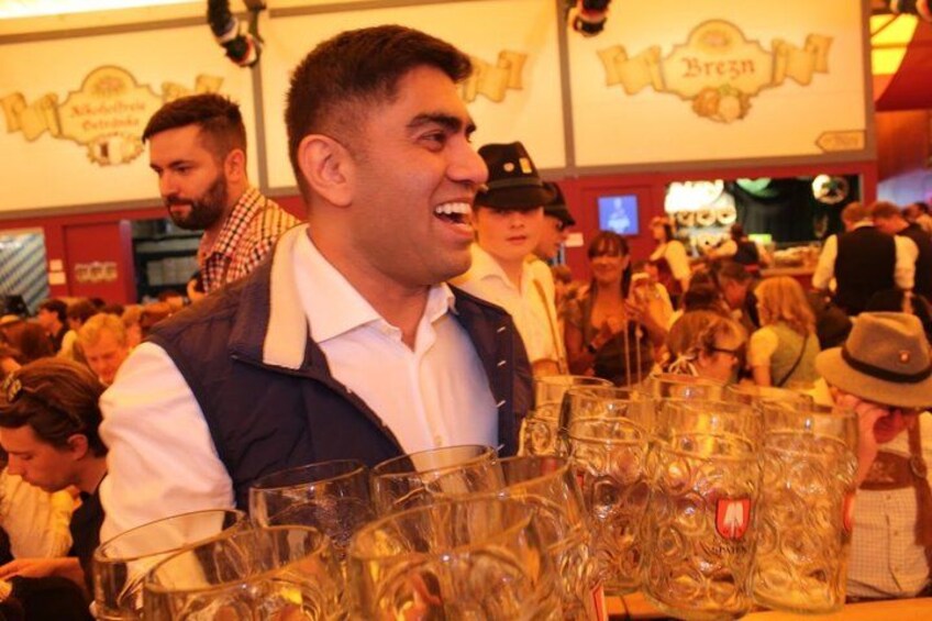 A person holding a tray of beer glasses in a crowded indoor setting. 5