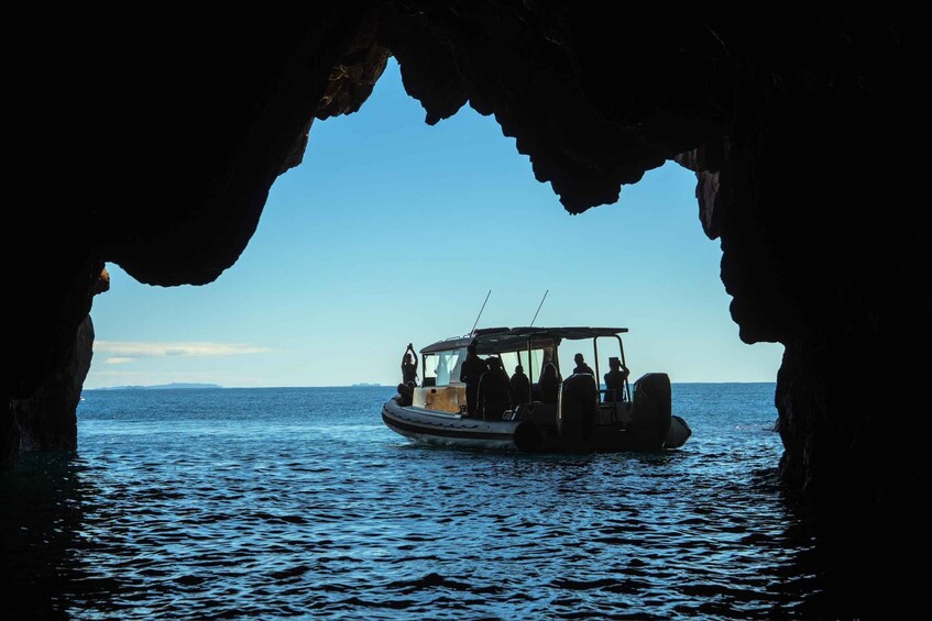 A boat with people on a calm sea, viewed through a cave opening. 2